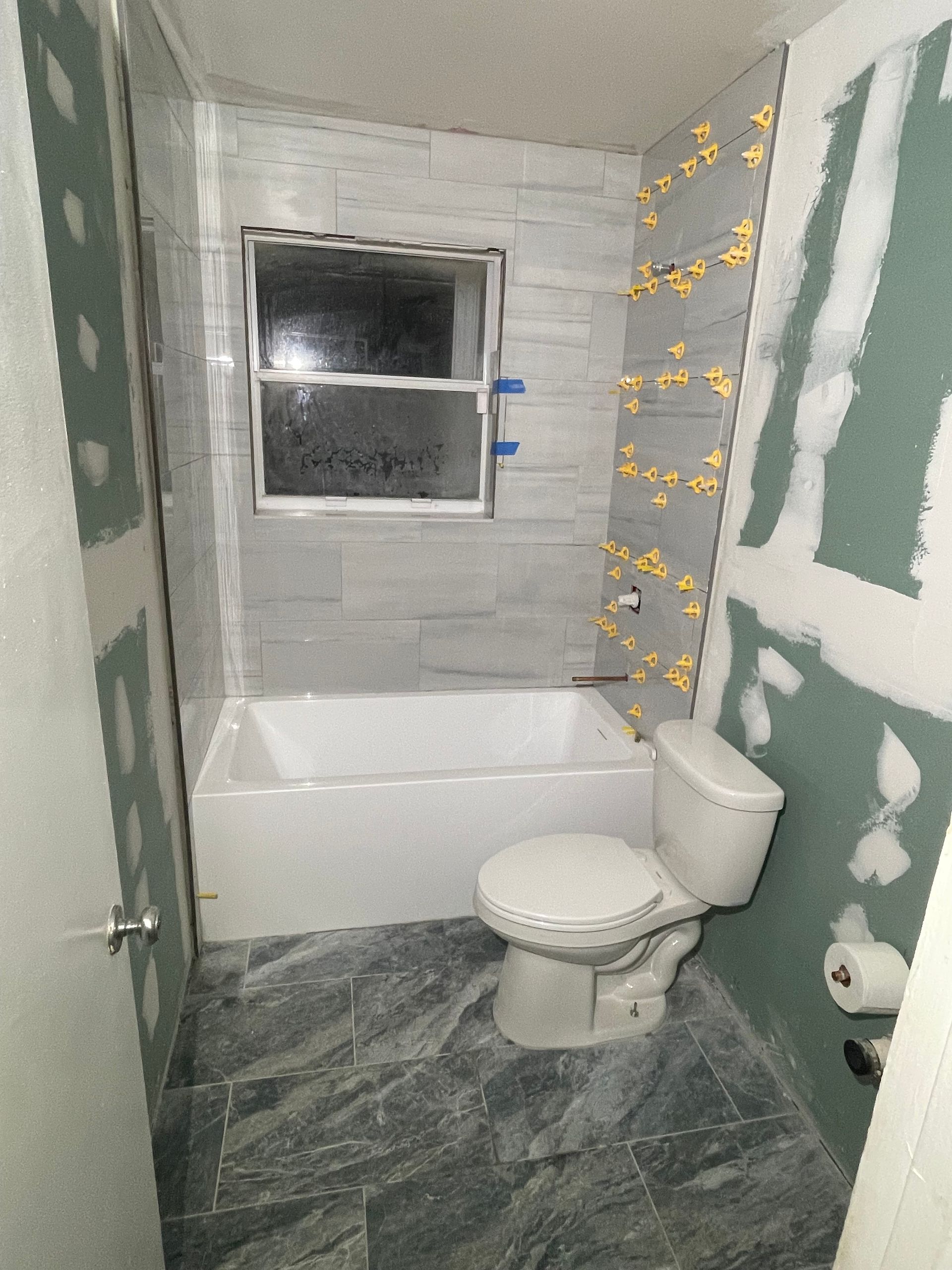 A bathroom with a toilet , tub and window under construction.