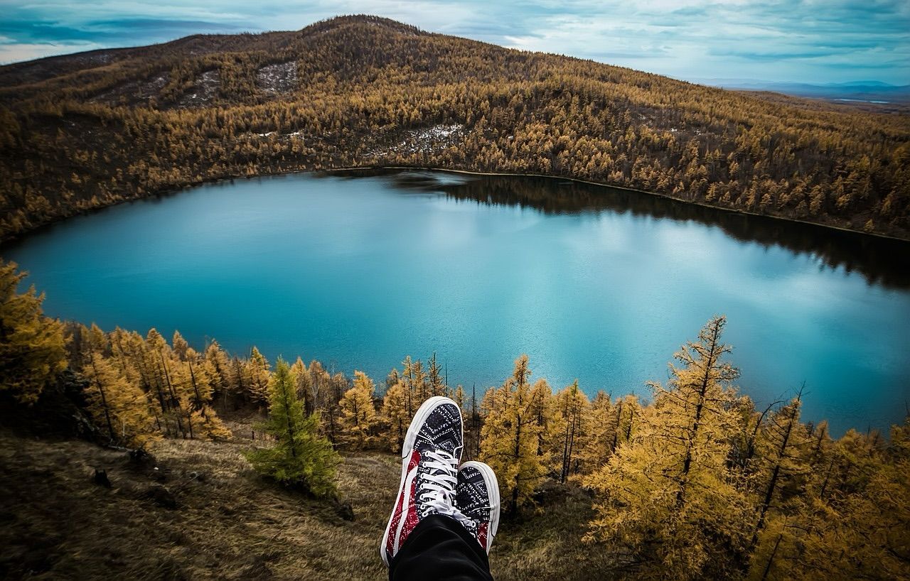 view of hiker's shoes overlooking a lake surrounded by fall colors