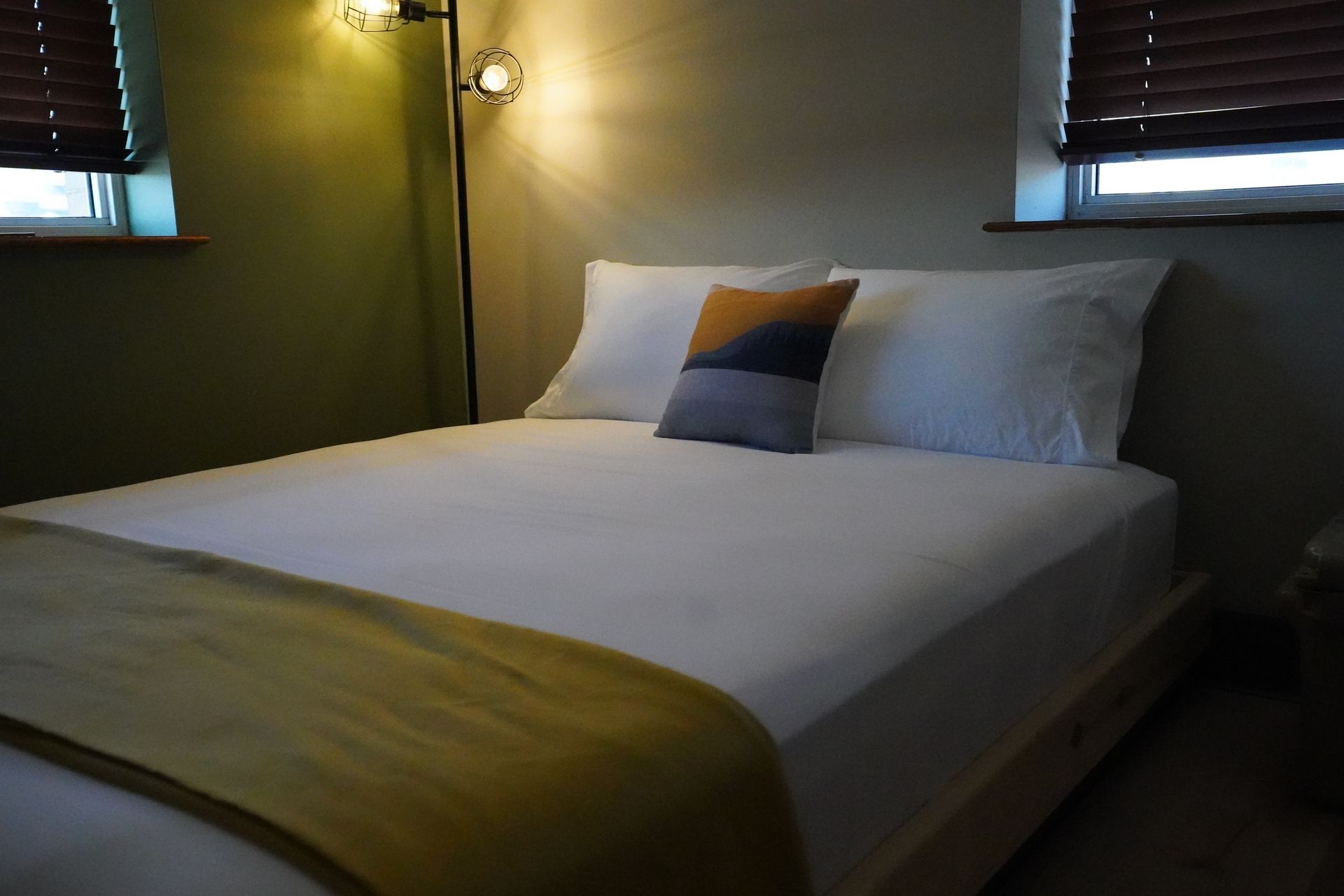 Bedroom with white bedding, patterned pillow, yellow throw, and floor lamp.