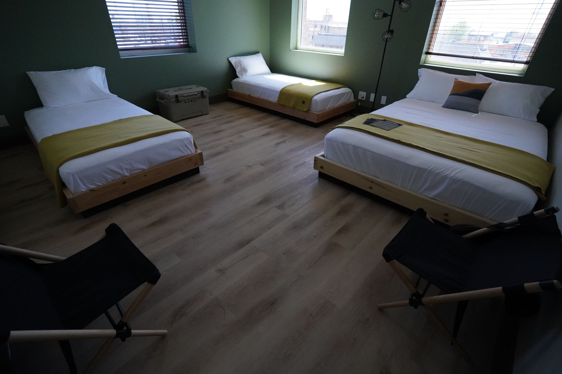 Bedroom with three beds, wooden floors, green walls, and two black folding chairs.
