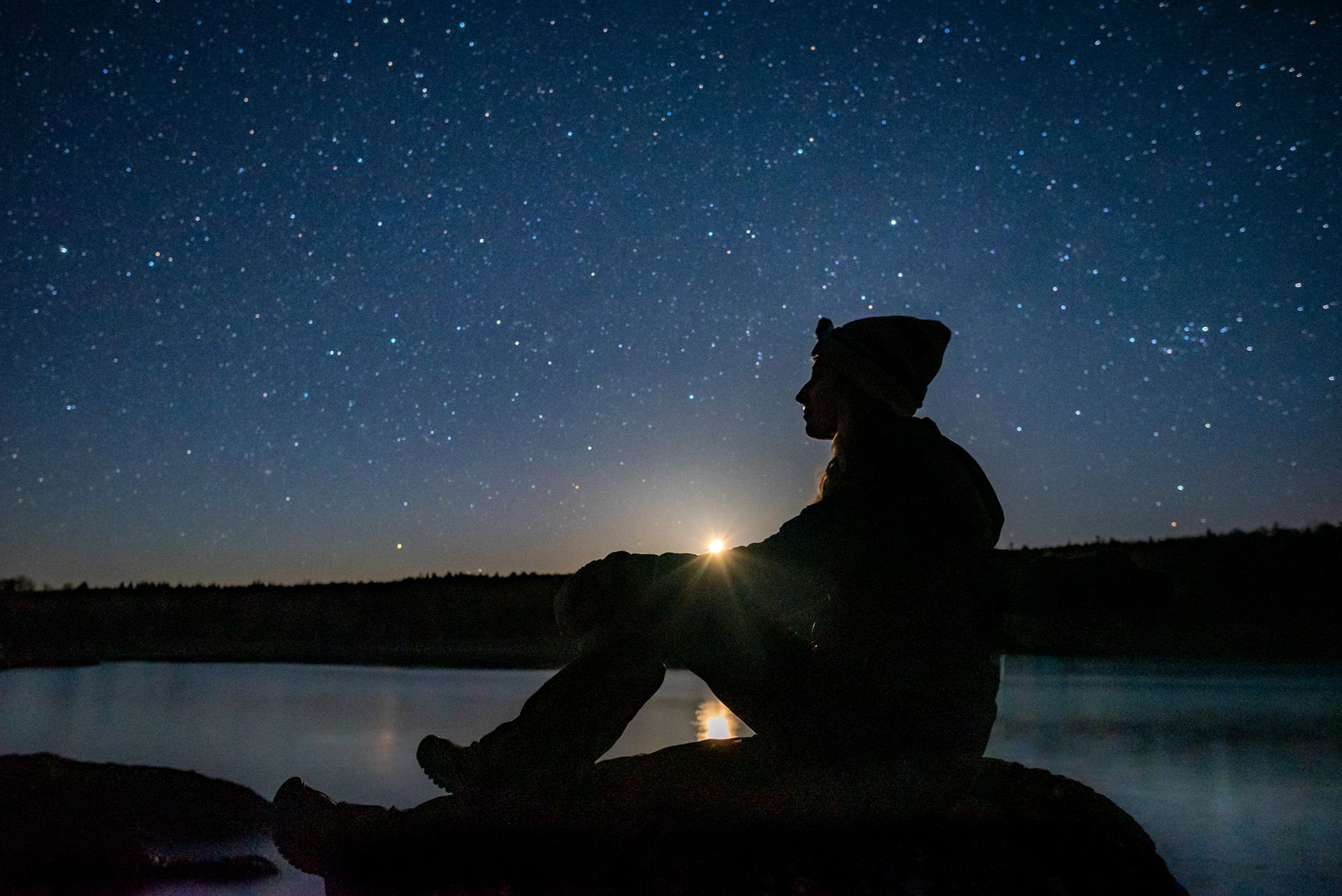 person's silhouette with sun fully set behind them and stars around