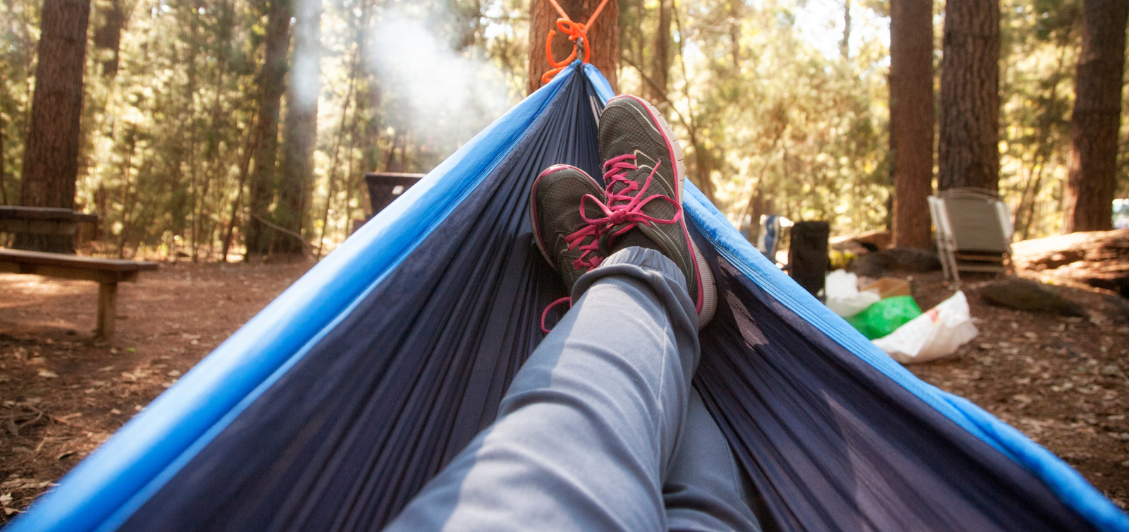 Person relaxing in a blue hammock in a forest, wearing hiking boots with pink laces.