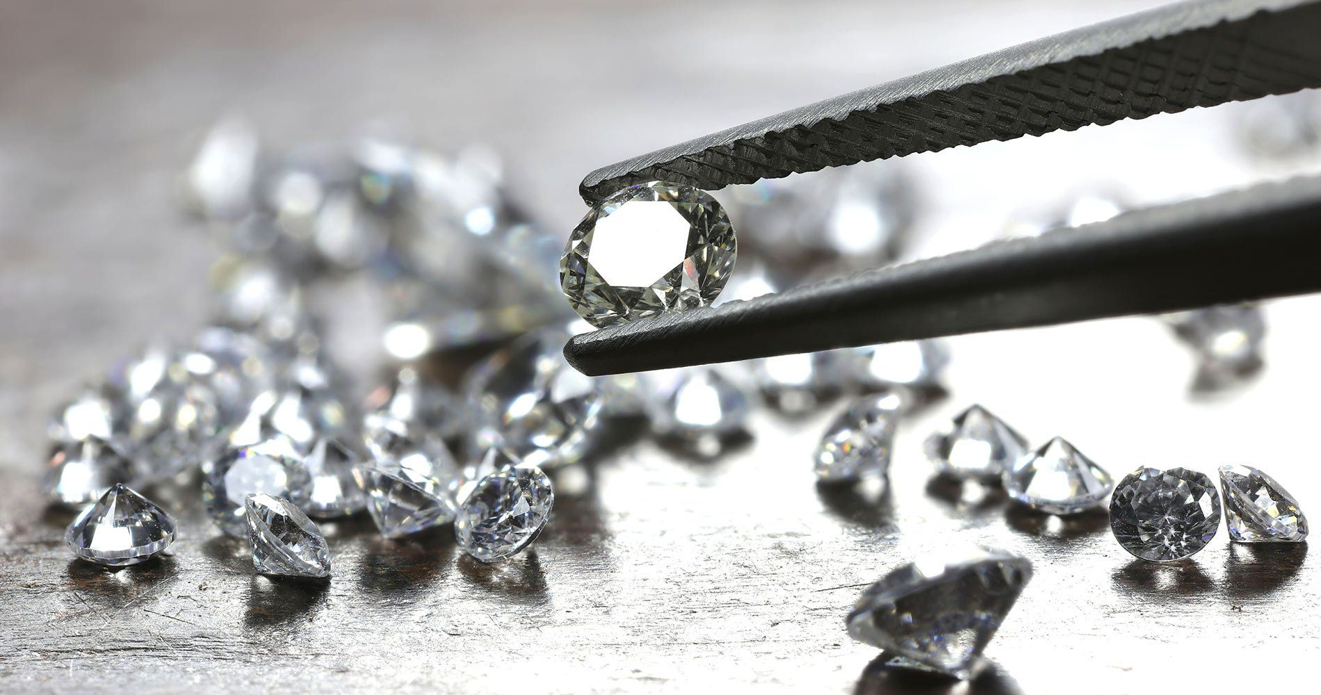 A pair of tweezers holding a diamond in front of a pile of diamonds.