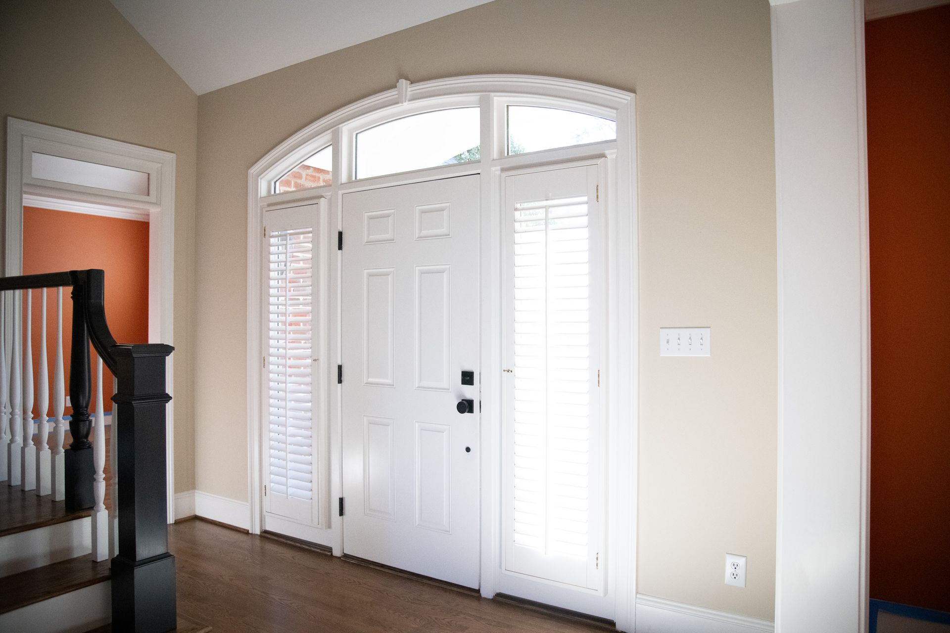 White front door with sidelights, arched transom, and tan walls.