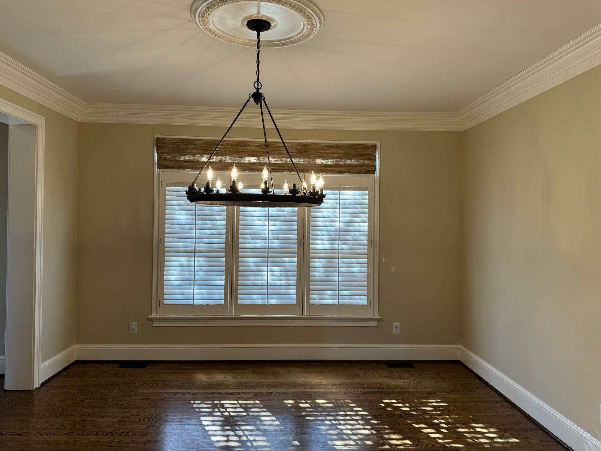 Empty dining room with chandelier, window, and hardwood floor. Neutral walls and trim.