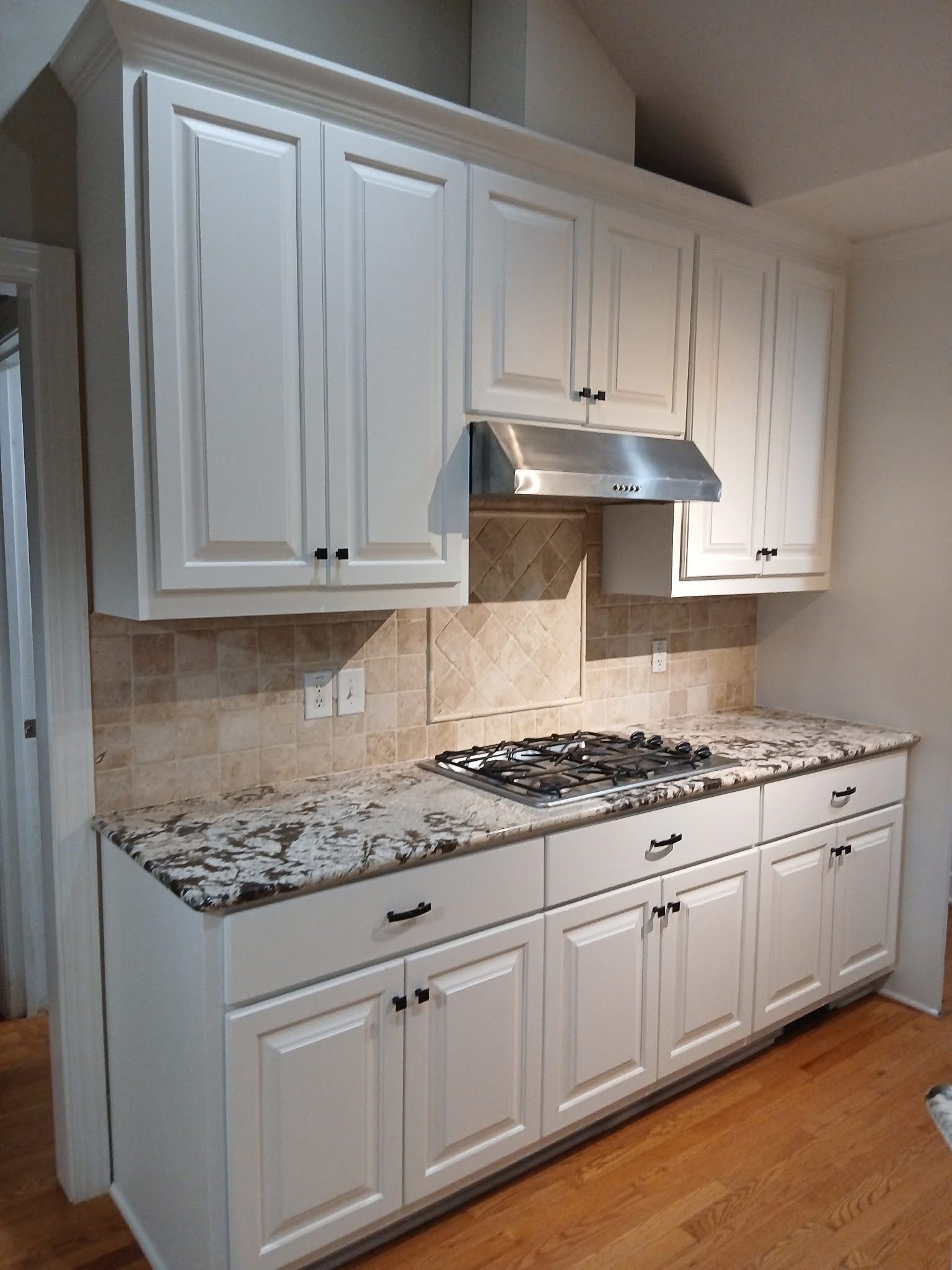 White kitchen cabinets with granite countertop, stovetop, and backsplash.