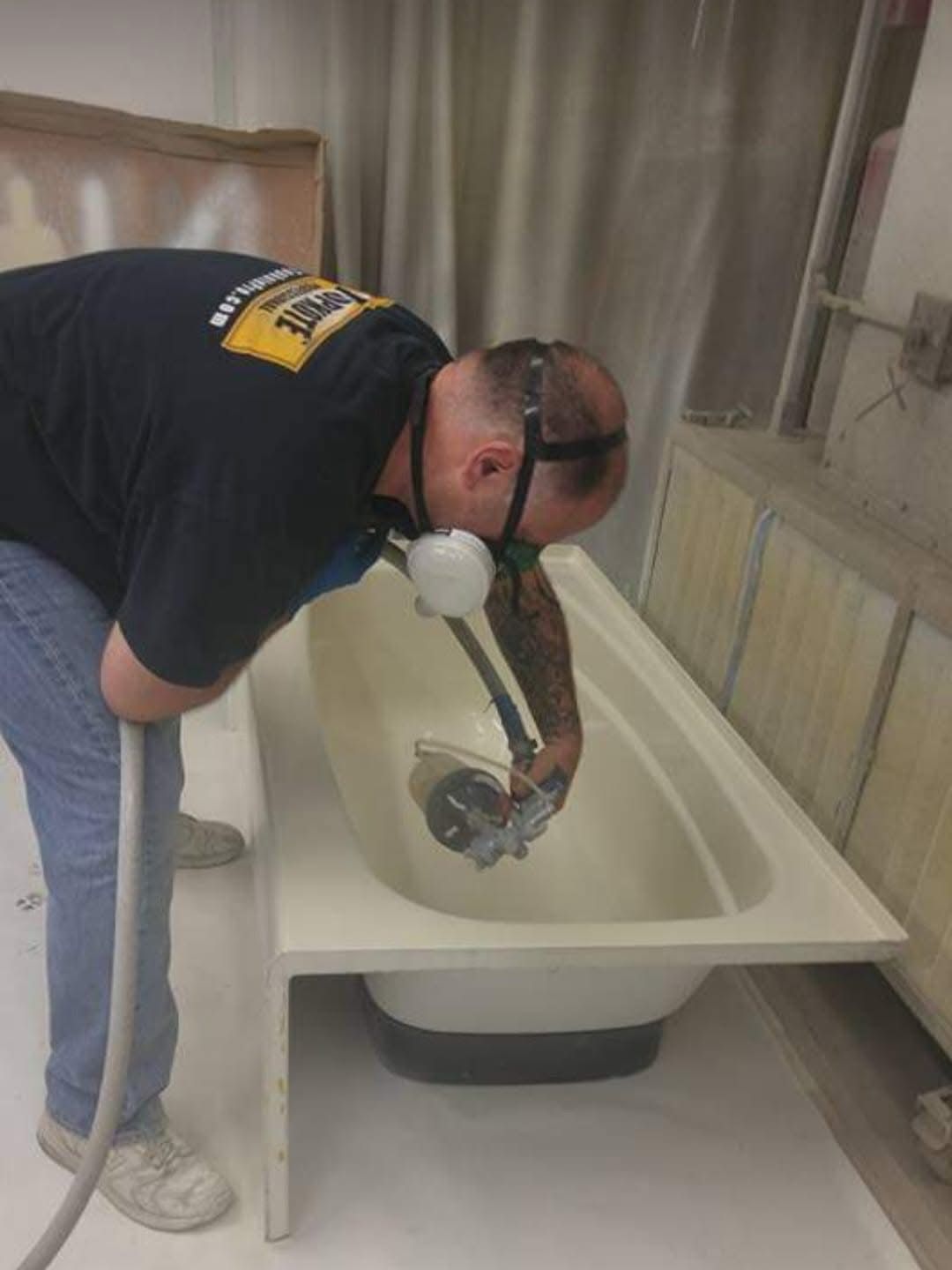 Man in respirator spraying bathtub in a workshop.