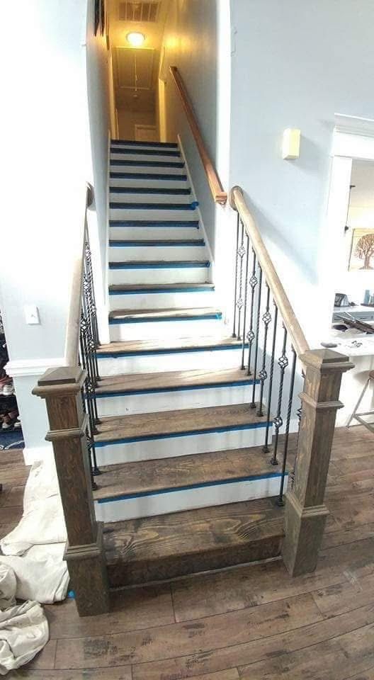 Staircase with wooden steps and railing, black iron balusters, and gray walls.