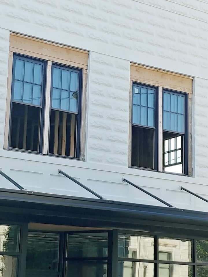 Two tall, blue-paned windows on a white brick building. Below, a dark awning with a glass window.