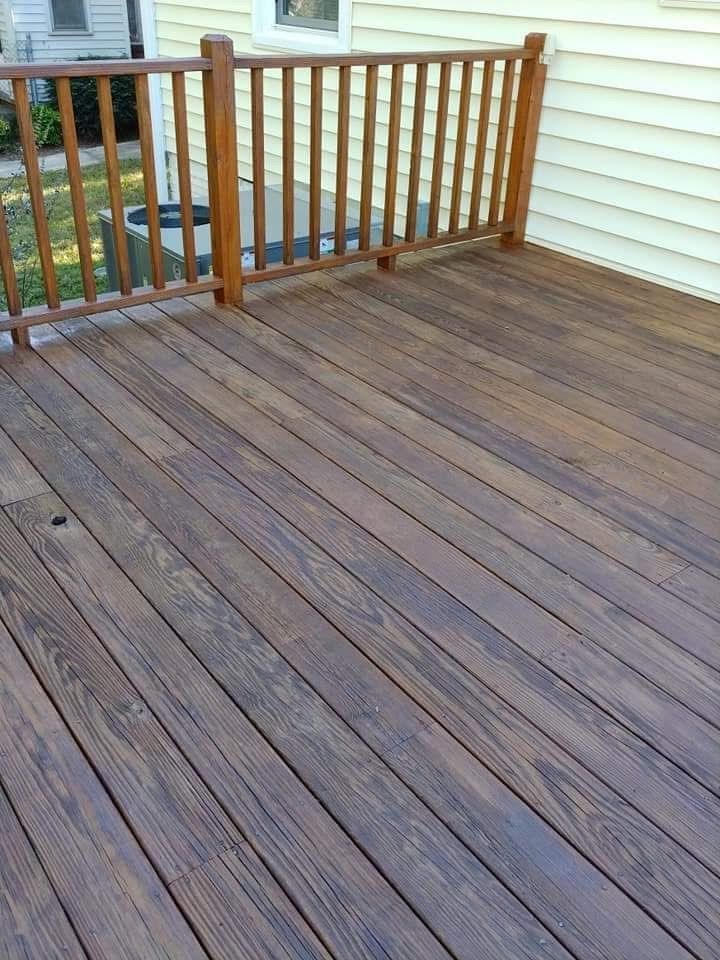 Wooden deck with brown stain, railing, and a light-colored house in the background.