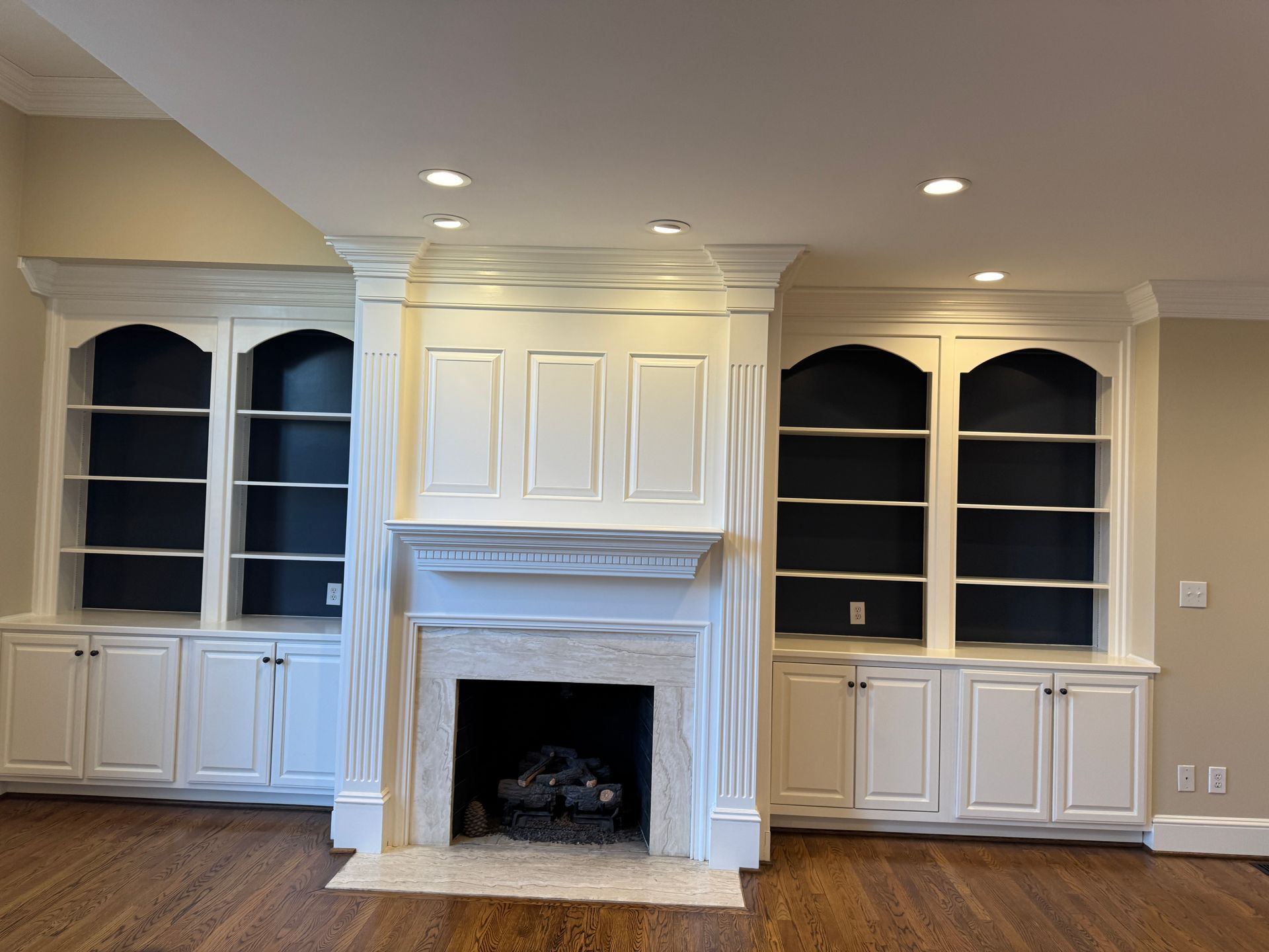 White fireplace flanked by built-in bookshelves with dark blue backs, in a room with hardwood floors.