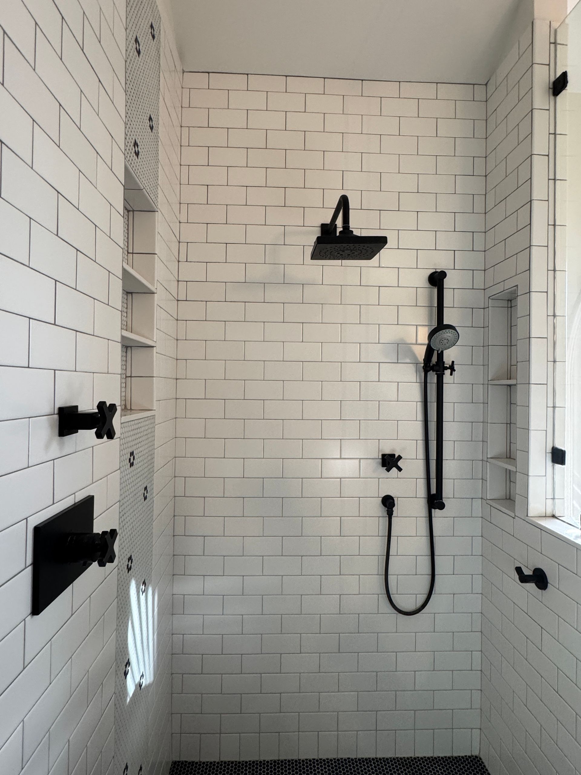 White tiled shower with black fixtures and a small window.