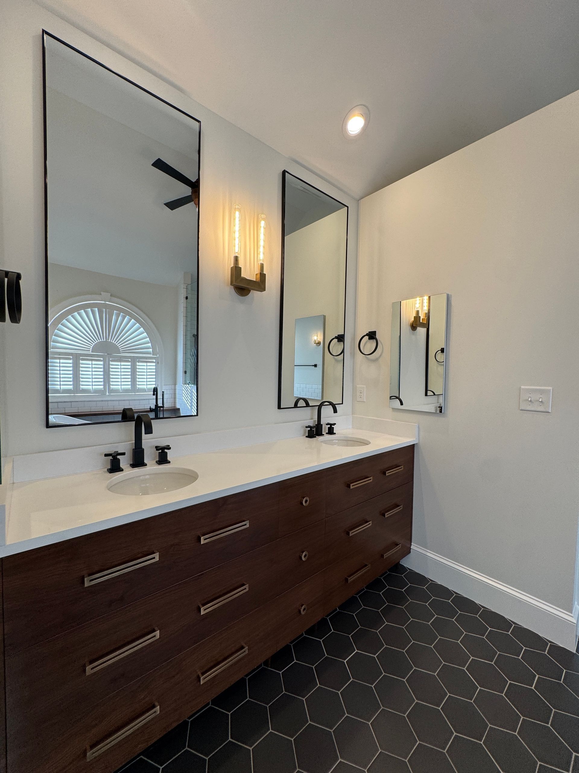 Modern bathroom with dark wood vanity, white countertop, black fixtures, hexagon tile floor, and large mirrors.