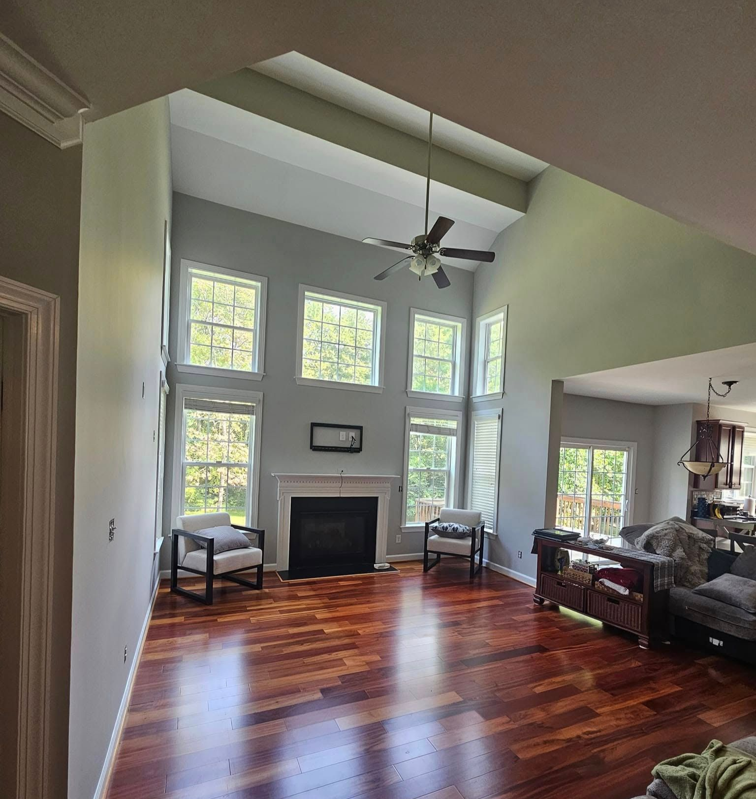 Living room with fireplace, hardwood floors, tall windows, and a ceiling fan.