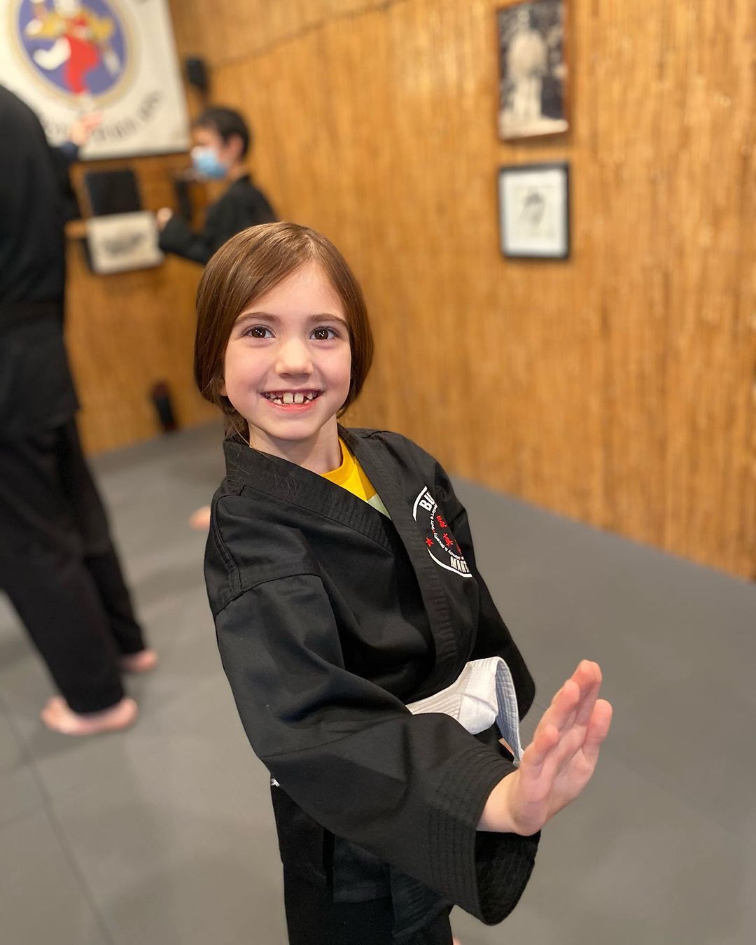 A young girl in a black karate uniform is smiling for the camera.
