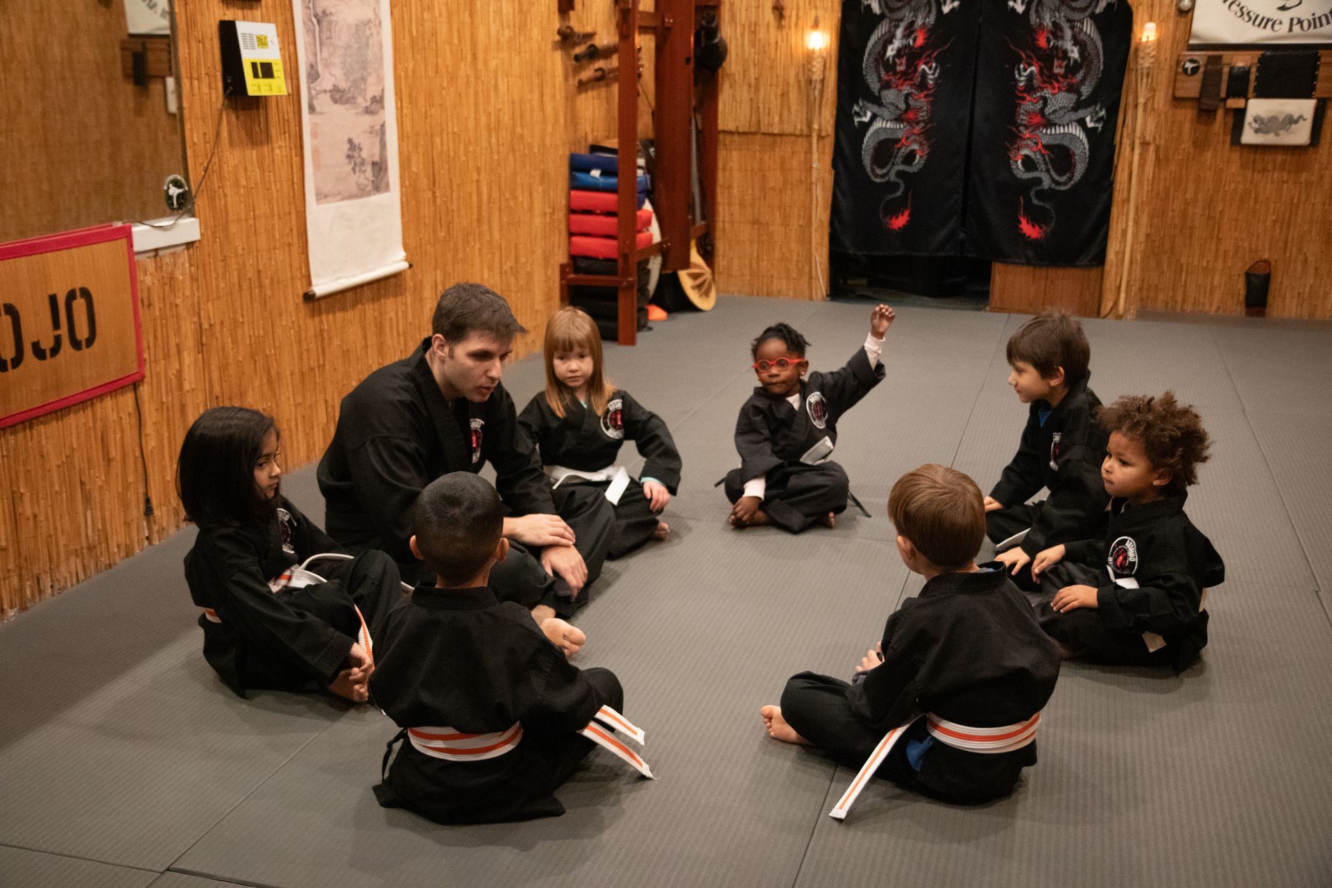 A group of children are sitting on the floor in a circle with a man talking to them.