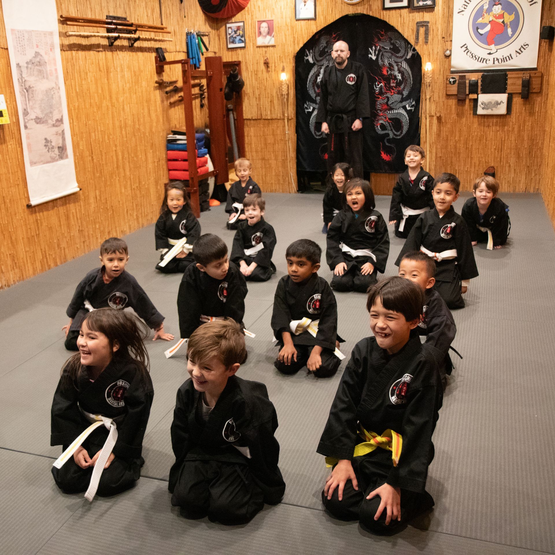 A group of children are kneeling on a mat in a room with a sign that says karate