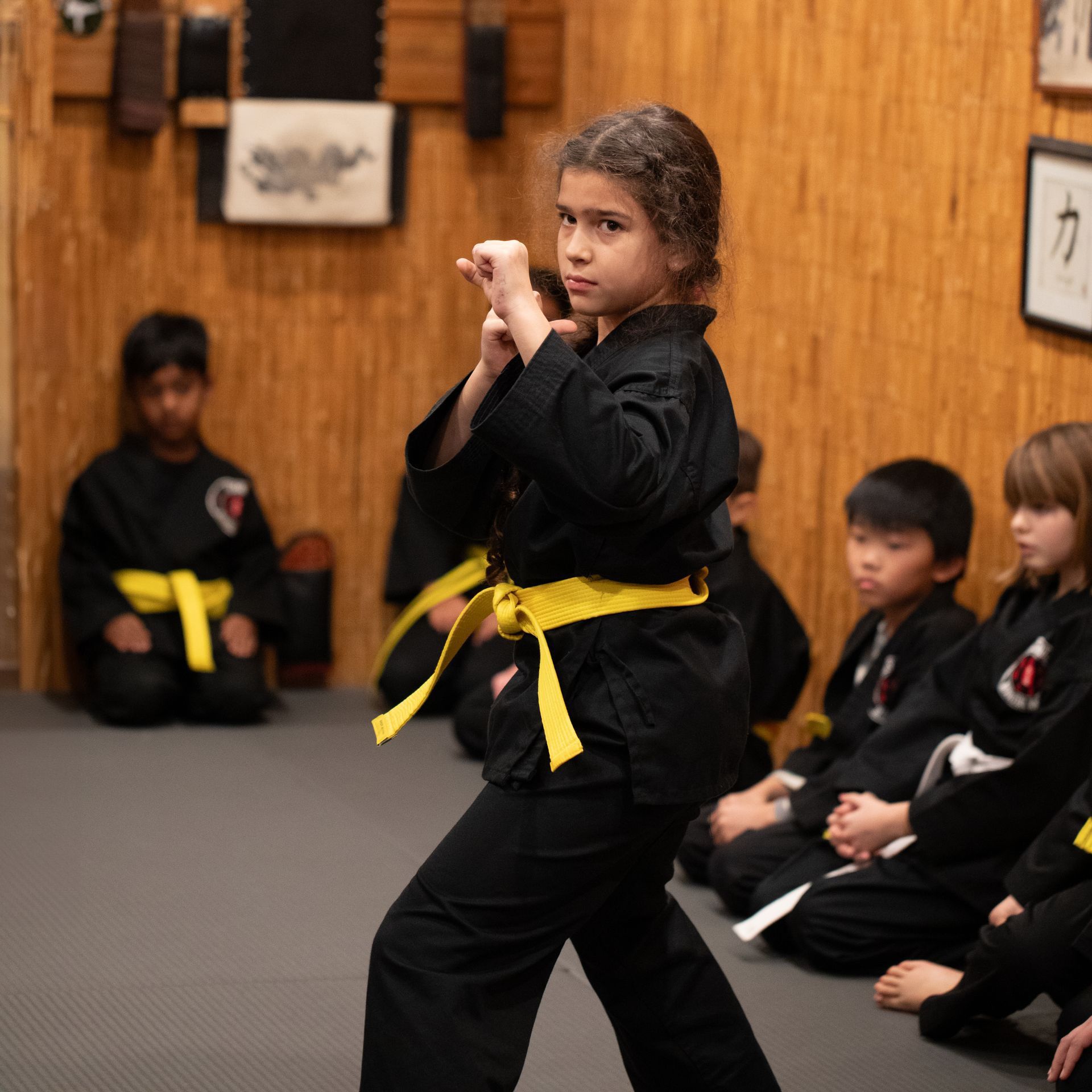 A young girl in a black karate uniform with a yellow belt