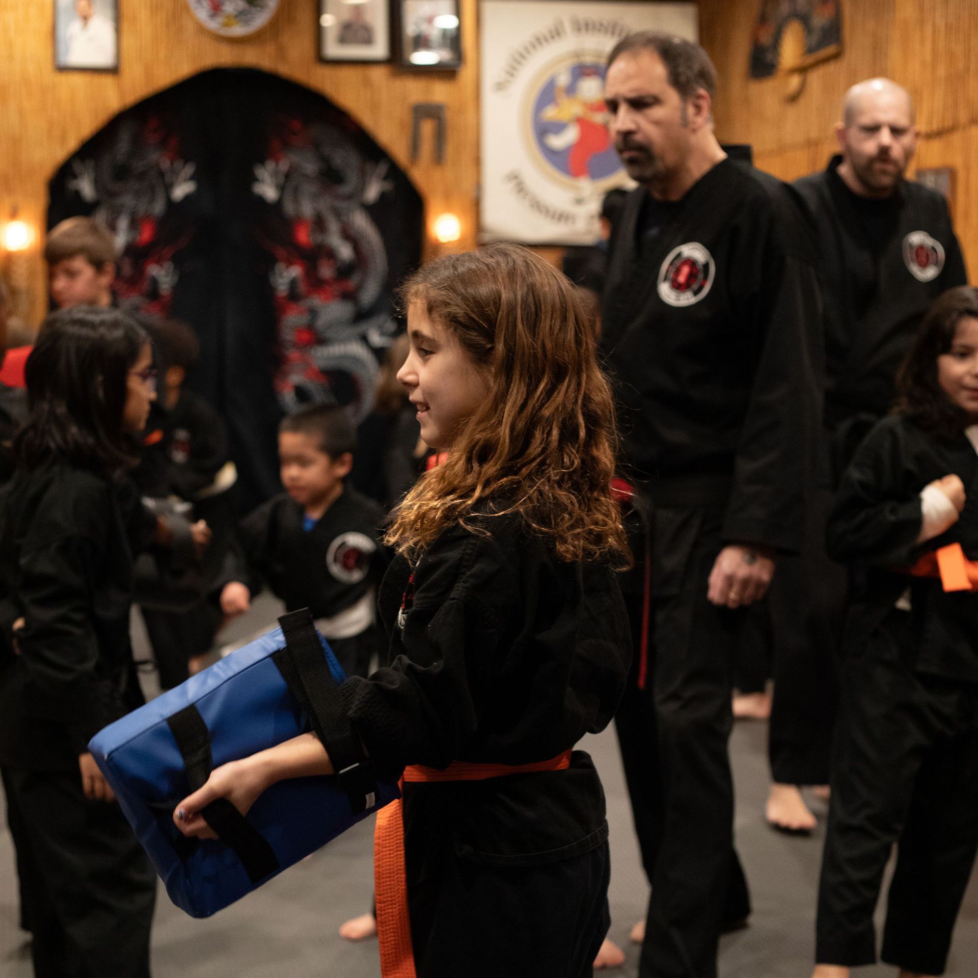 A girl in a black karate uniform is holding a blue bag