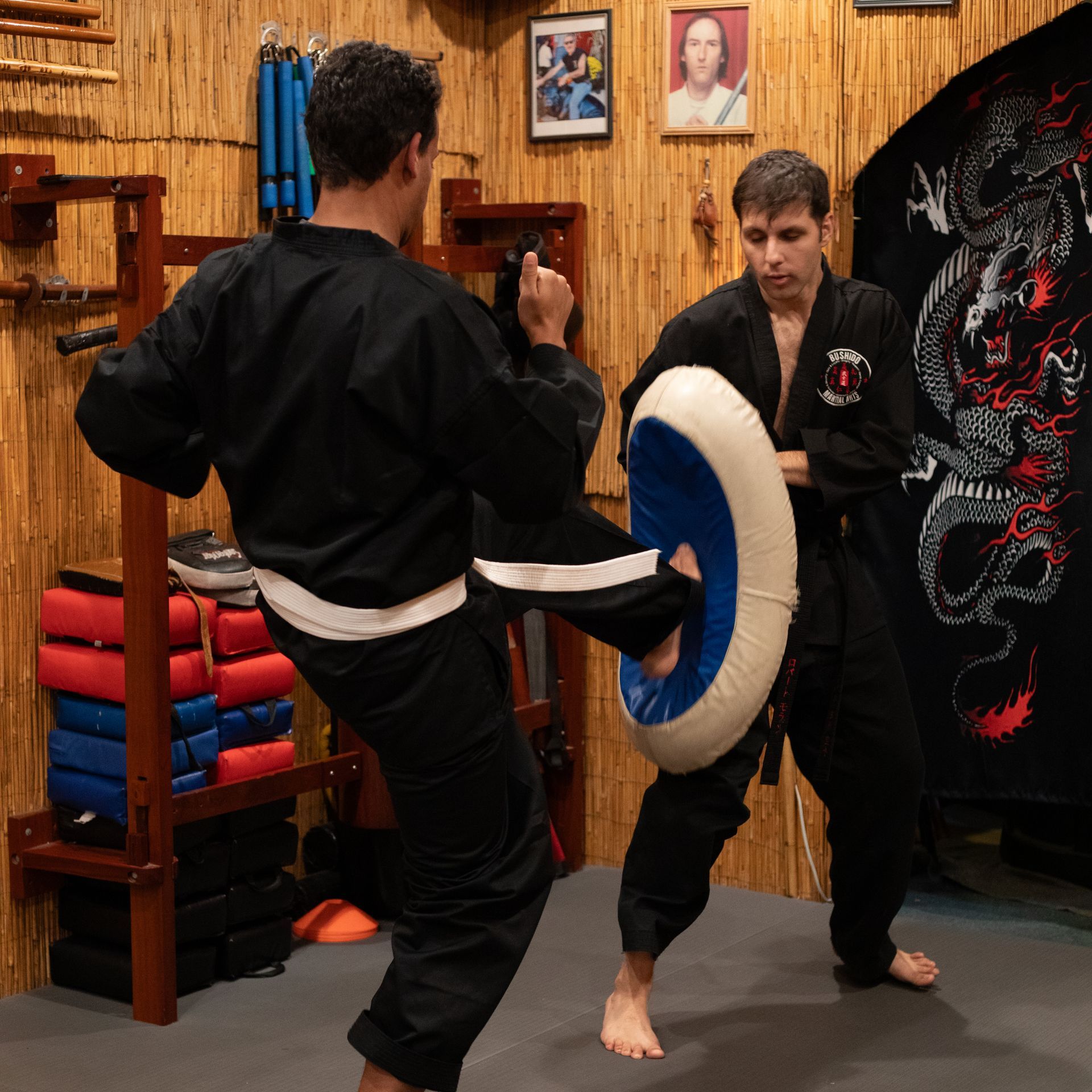 Two men are practicing martial arts in a room with a dragon on the wall