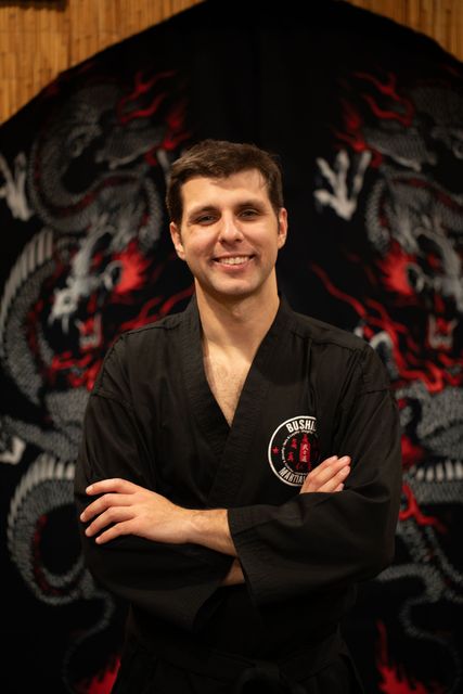 a man in a black karate uniform is smiling with his arms crossed .