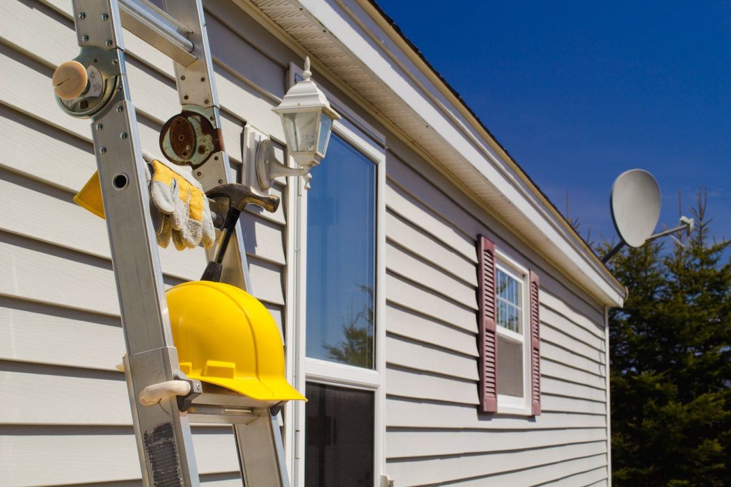A yellow hard hat is hanging from a ladder on the side of a house.