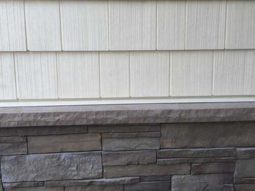 A close up of a stone wall with a white siding on a house.