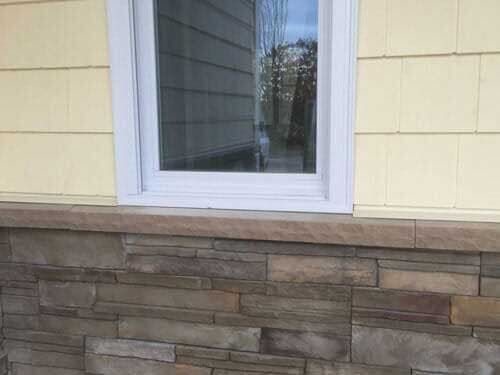 A window on the side of a house with a stone wall.