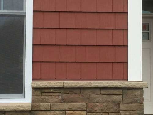 A close up of a red siding on a house with a stone wall.