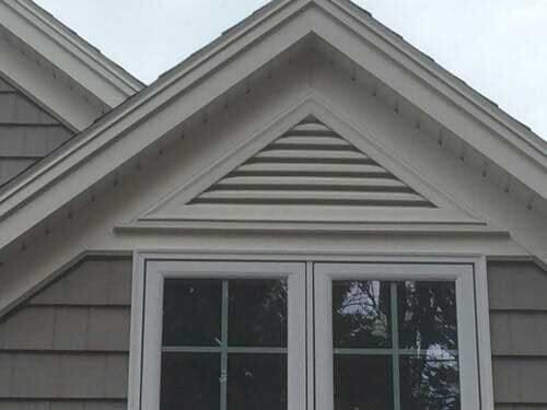 A window on the side of a house with a triangle shaped roof.