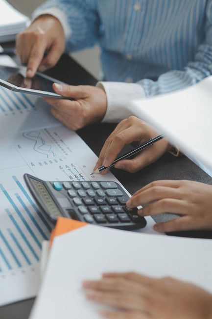 Manos trabajando con una calculadora, papeles y una tableta en un escritorio, posiblemente de contabilidad o finanzas.