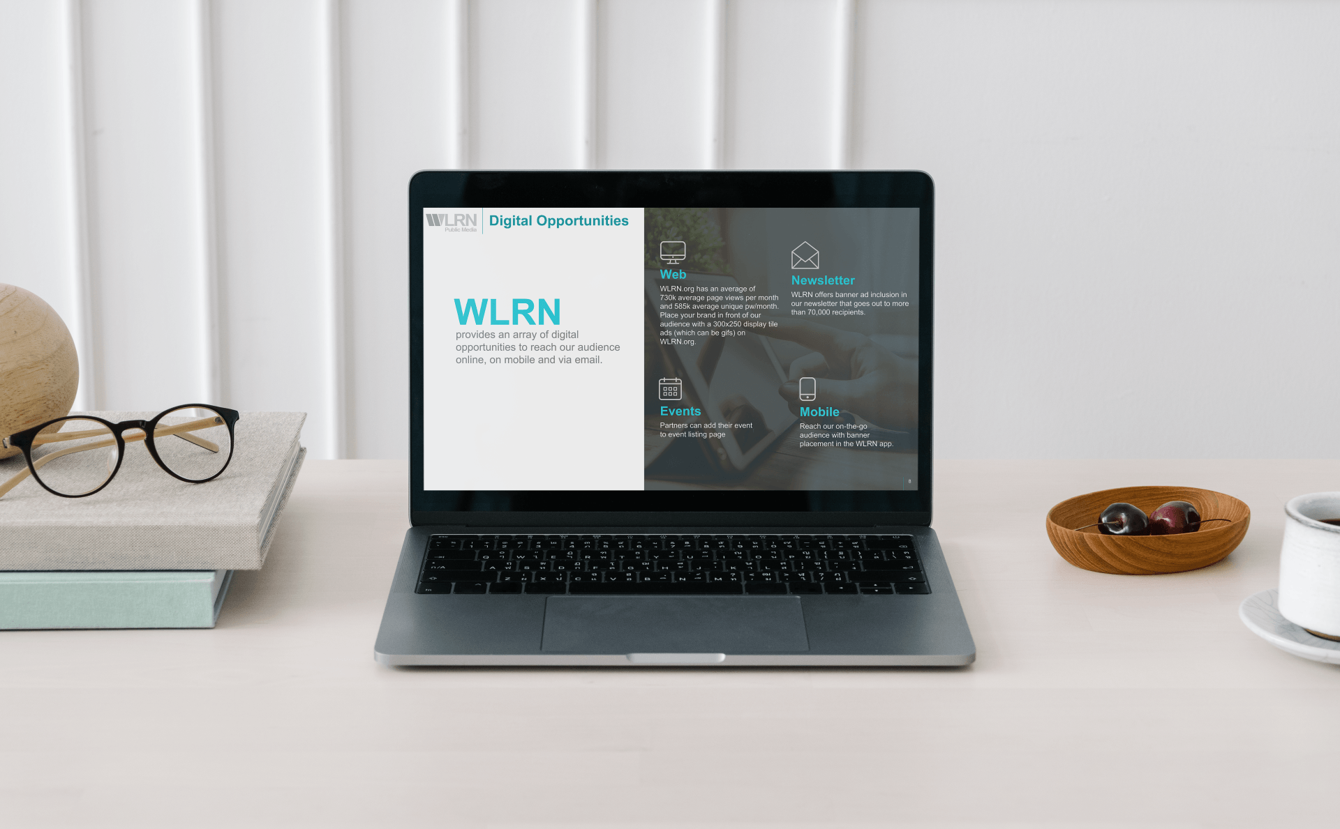 A laptop computer is sitting on a desk next to a stack of books and glasses.