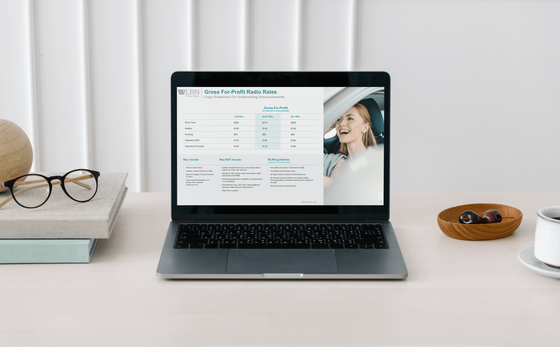 A laptop computer is sitting on a desk next to a stack of books and glasses.
