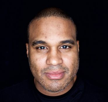 A man with a beard is looking at the camera with a black background