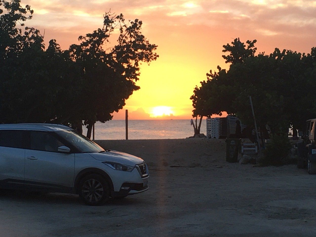 A car is parked in front of a sunset over the ocean.