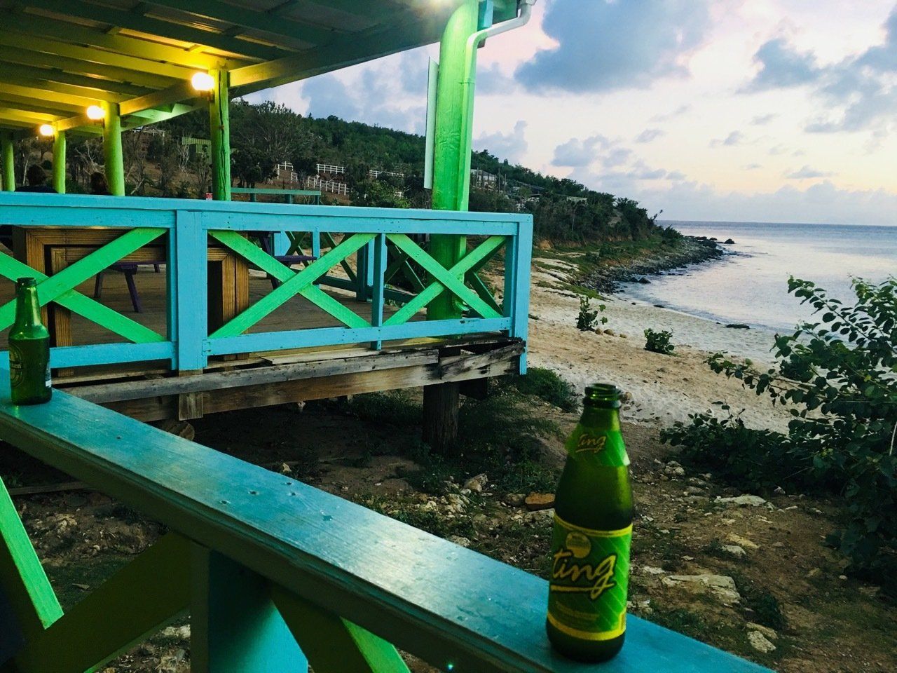 A bottle of beer is sitting on a wooden railing overlooking the ocean.
