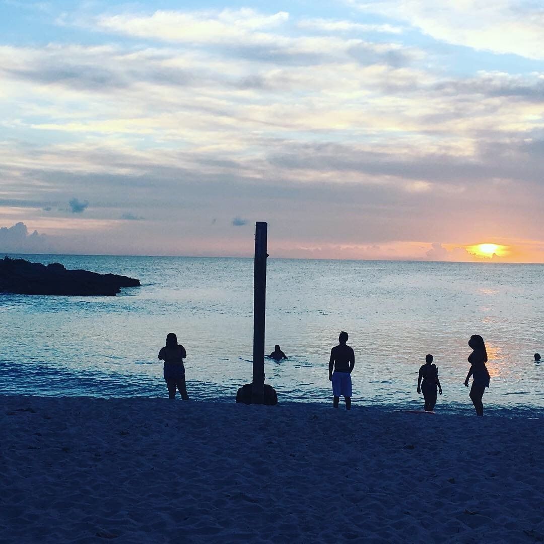 A group of people standing on a beach at sunset