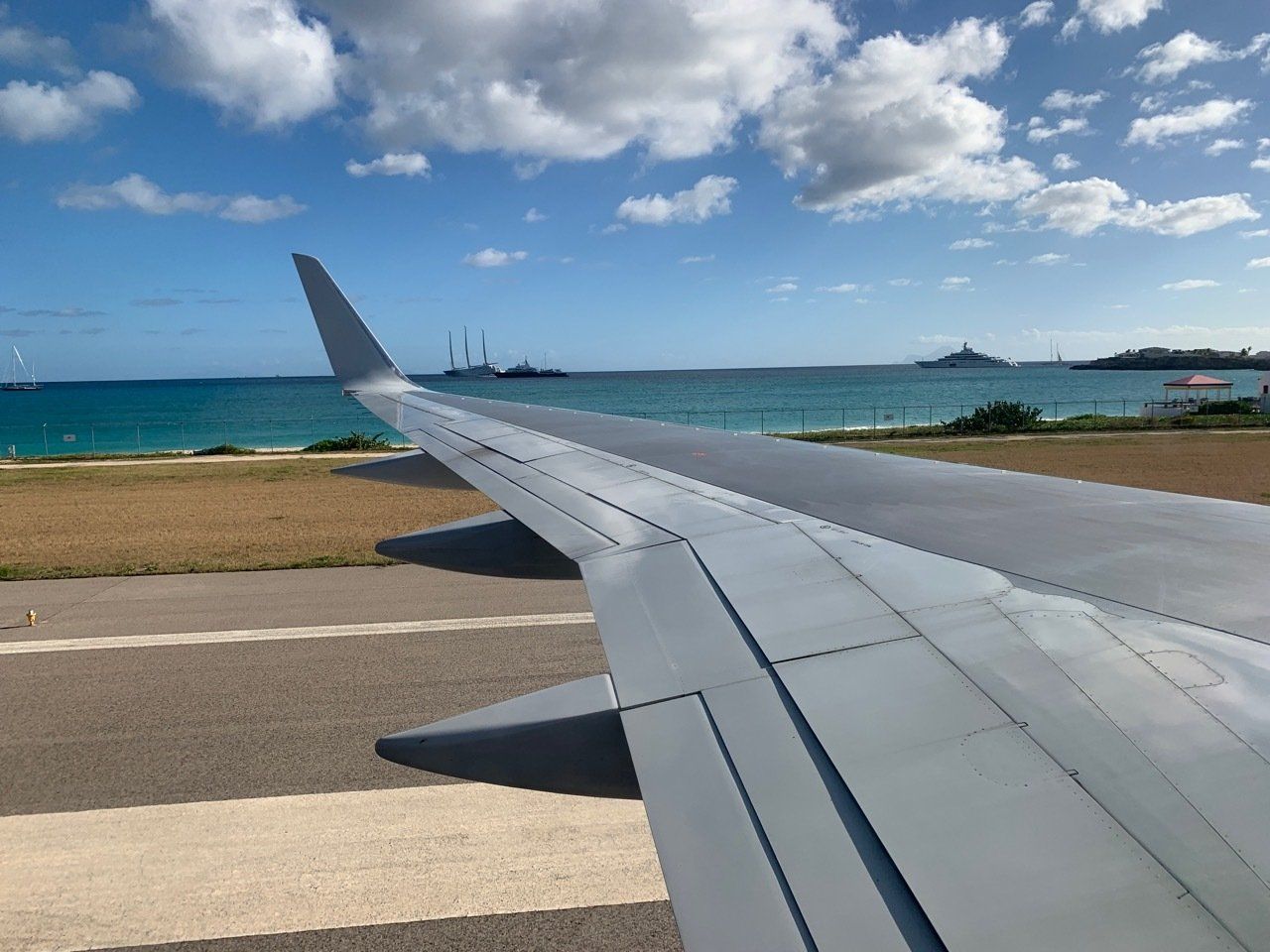 The wing of an airplane is sitting on a runway overlooking the ocean.