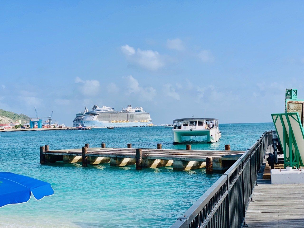 A boat is docked at a pier with a cruise ship in the background.