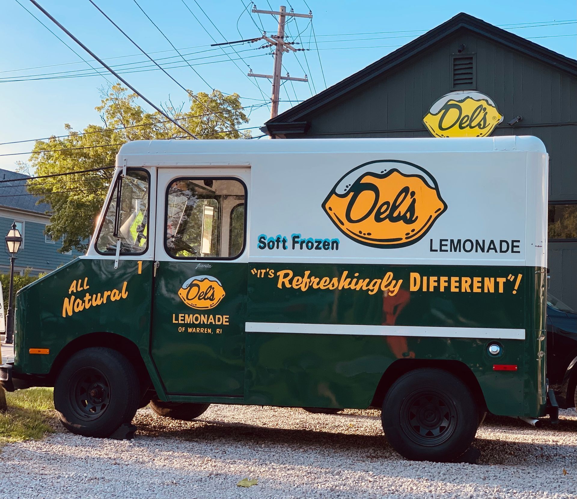 A green and white Del 's lemonade truck is parked in front of a building