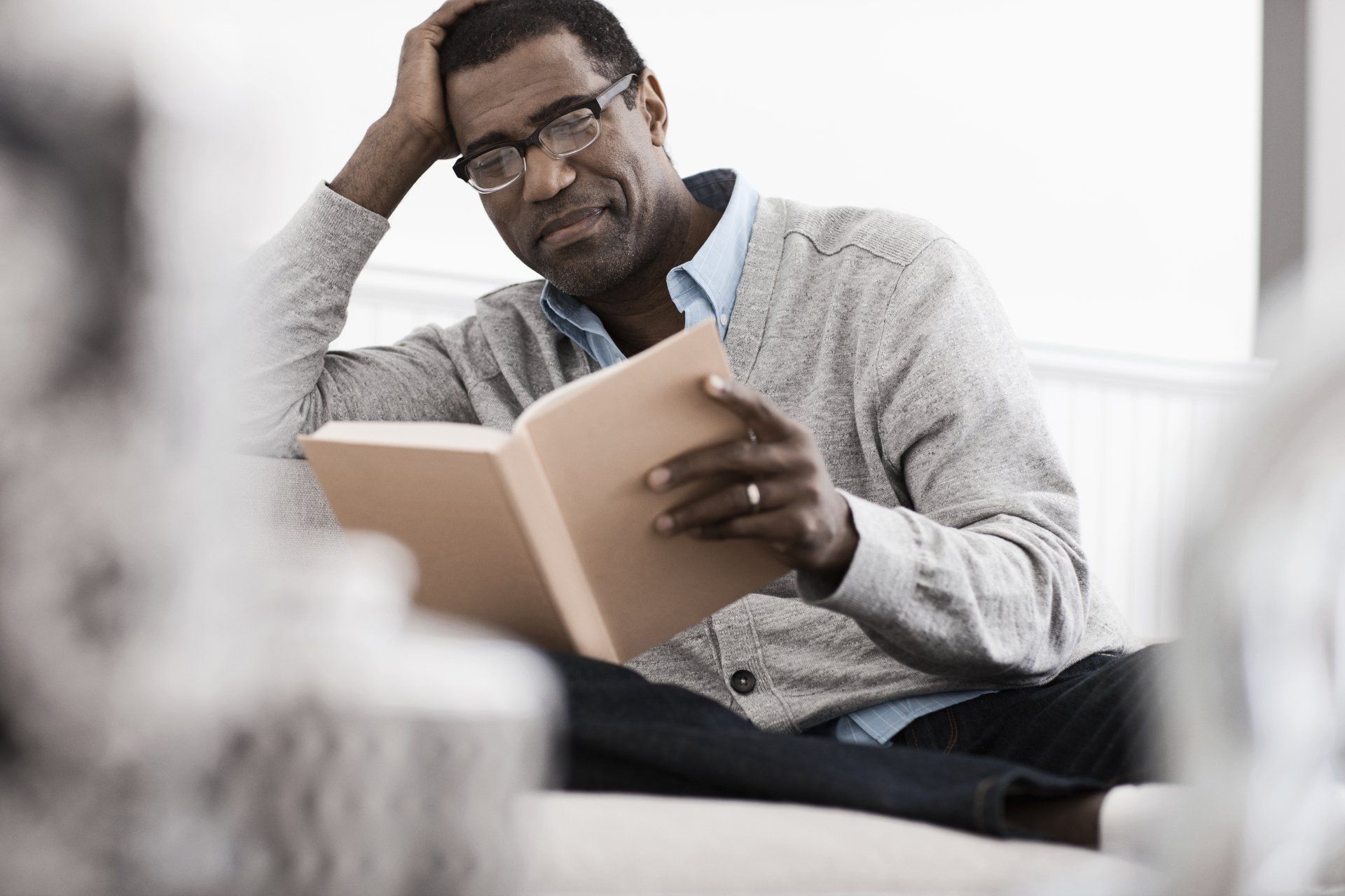 A man is sitting on a couch reading a book.