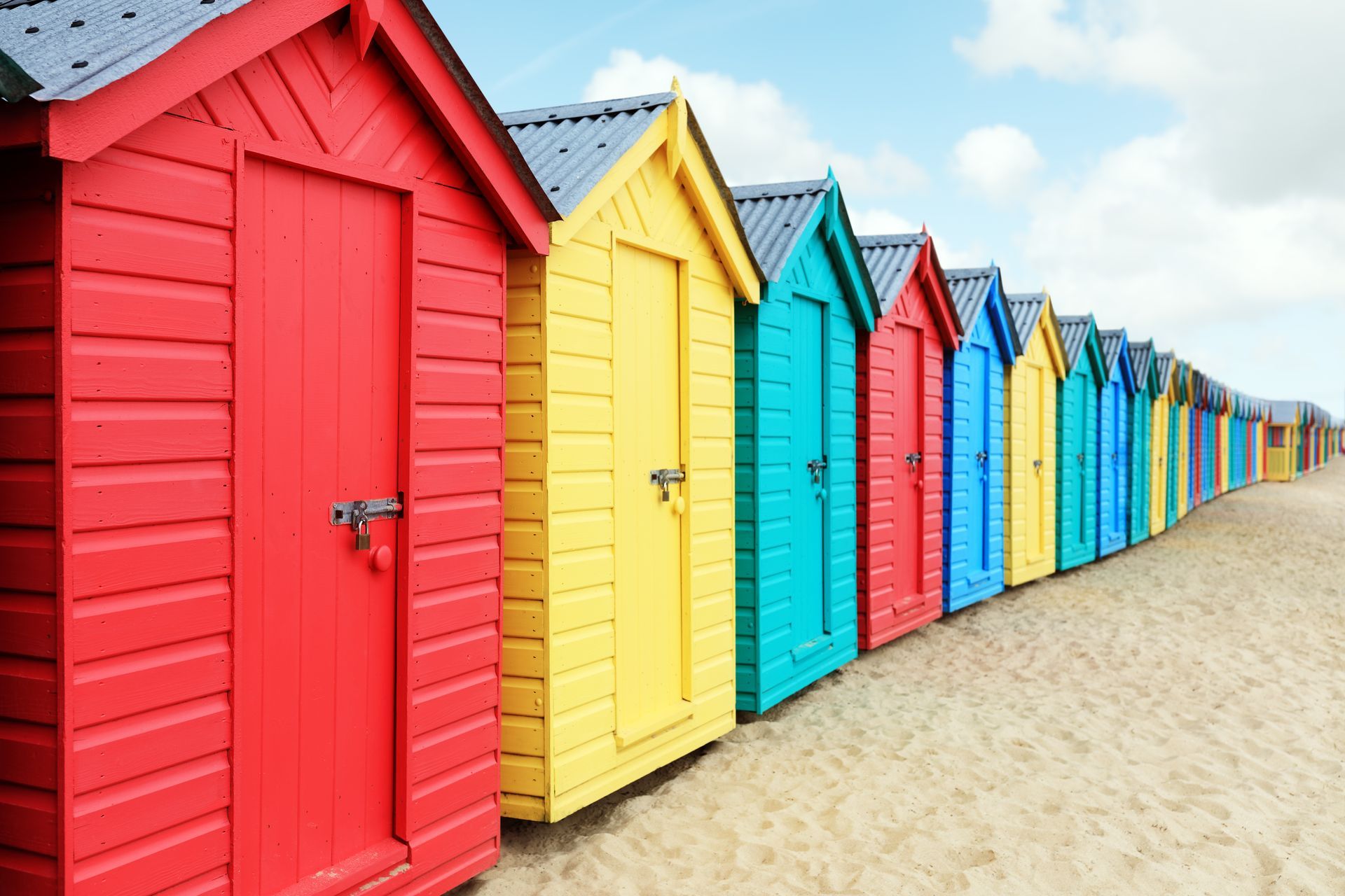 A row of colorful beach huts on a sandy beach.
