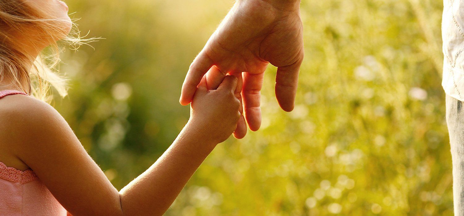 A little girl is holding a man 's hand in a field.