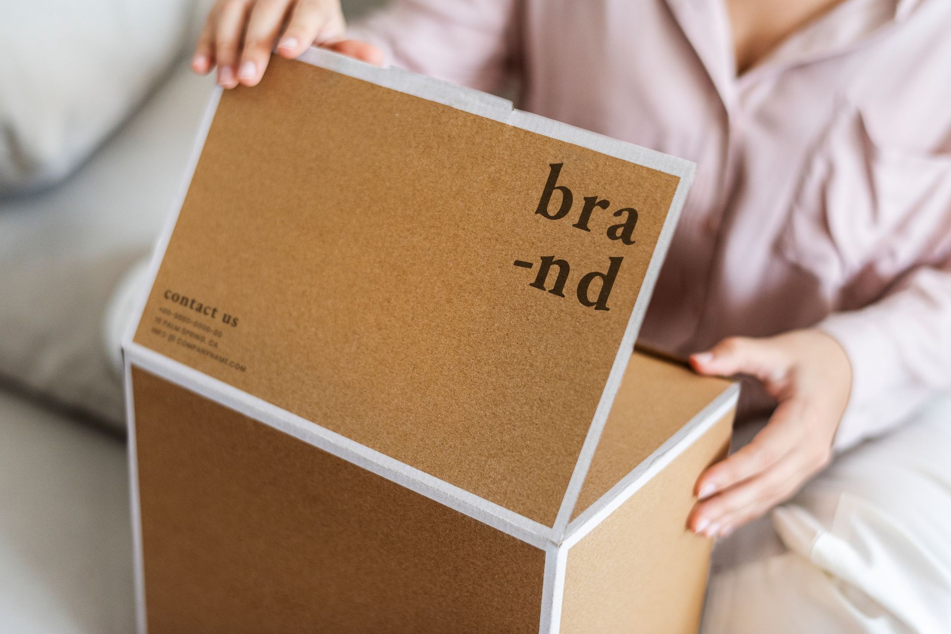 A woman is sitting on a couch holding a cardboard box with the lid open.