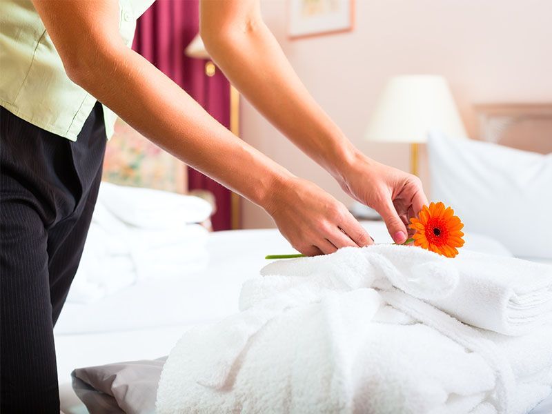 A woman is putting a flower on a bed in a hotel room.