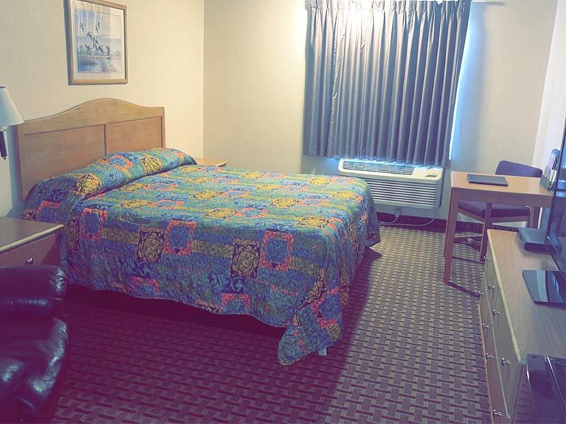 A hotel room with a bed, desk, chair and television