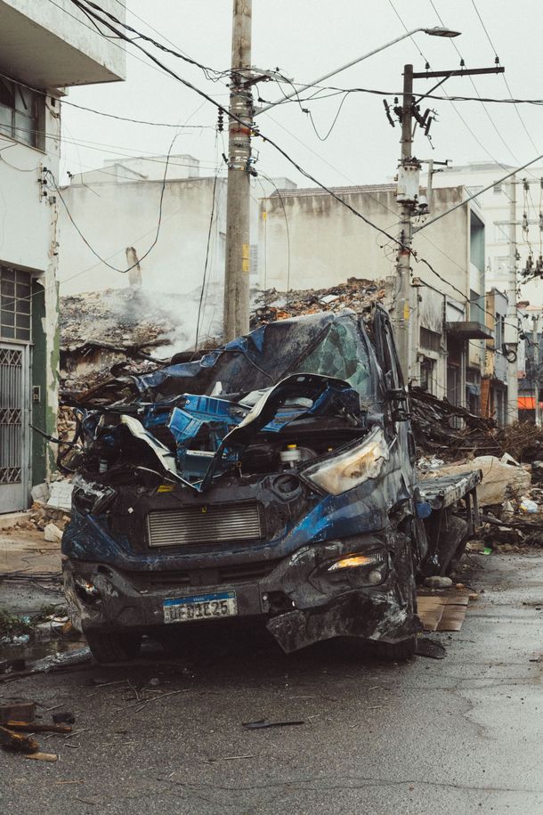 Severely damaged blue car crumpled on a wet street in a residential area, with power lines overhead