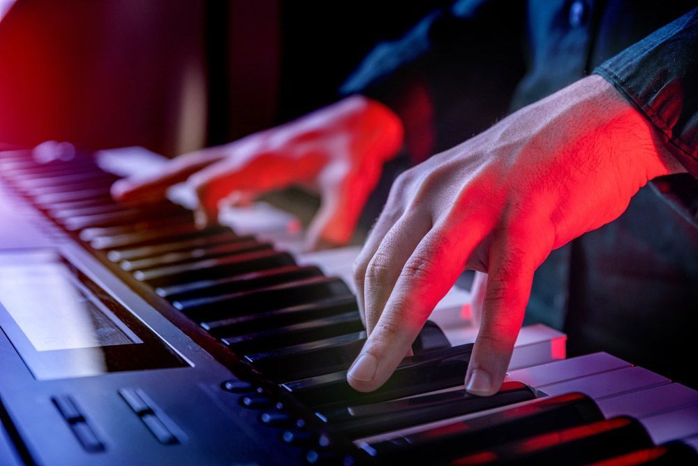 Hands Playing A Keyboard Under Red And Blue Stage Lighting — Kennedy Amplifier Hire Service In South Mackay, QLD