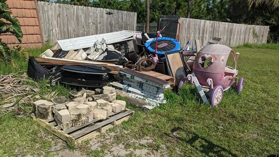 A pile of trash in a backyard with a pink toy car and a trampoline.