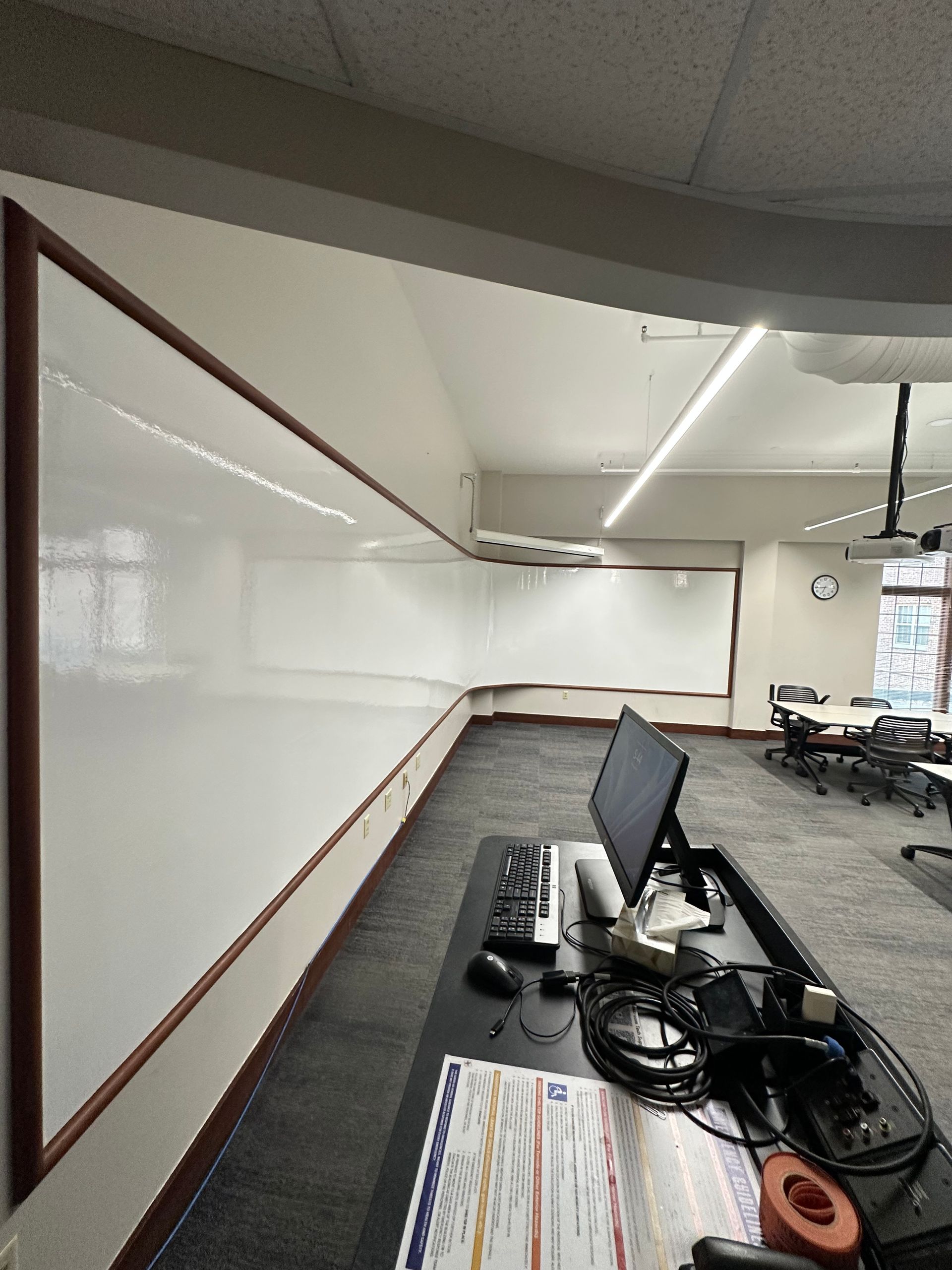 Empty classroom with whiteboard wall, desks, and a monitor on the front table